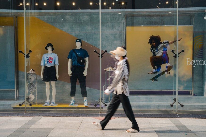 epa10790164 A woman walks by in front of the shop window of a clothing store in Beijing, China, 08 August 2023. China&#039;s trade surplus dropped to 80.6 billion US dollar (73.36 billion Euro) in Jul ...