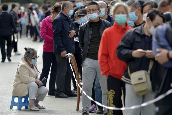 A woman wearing a face mask to help curb the spread of the coronavirus sits on a stool as masked residents line up for the COVID-19 test near the residential area in Qingdao in east China&#039;s Shand ...