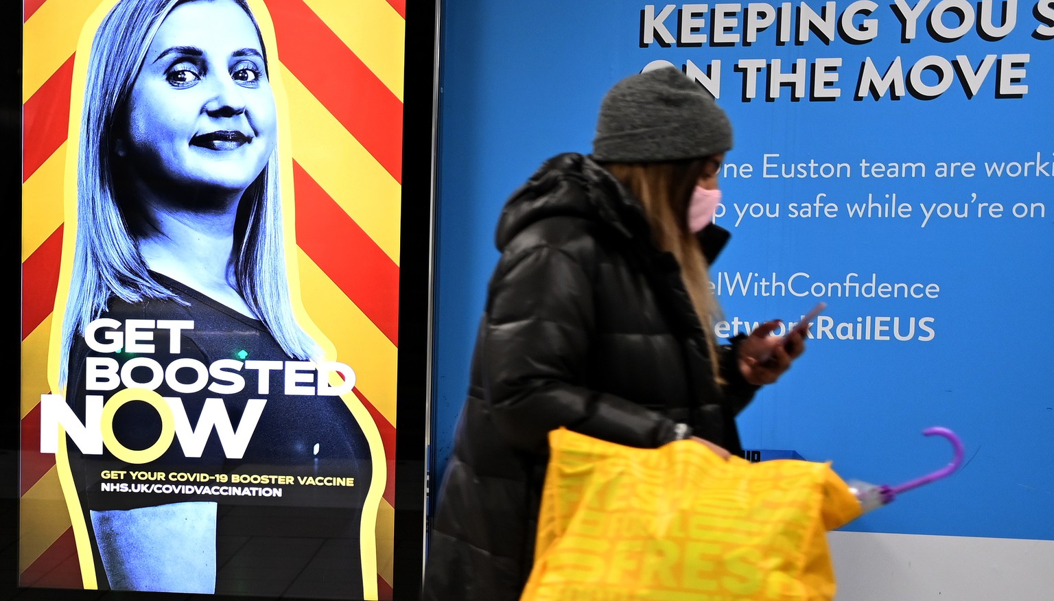 epa09655946 A woman walks past a COVID-19 vaccine &#039;booster&#039; campaign advertisement at Euston Station in London, Britain, 24 December 2021. Many Britons will be self testing for COVID-19 this ...