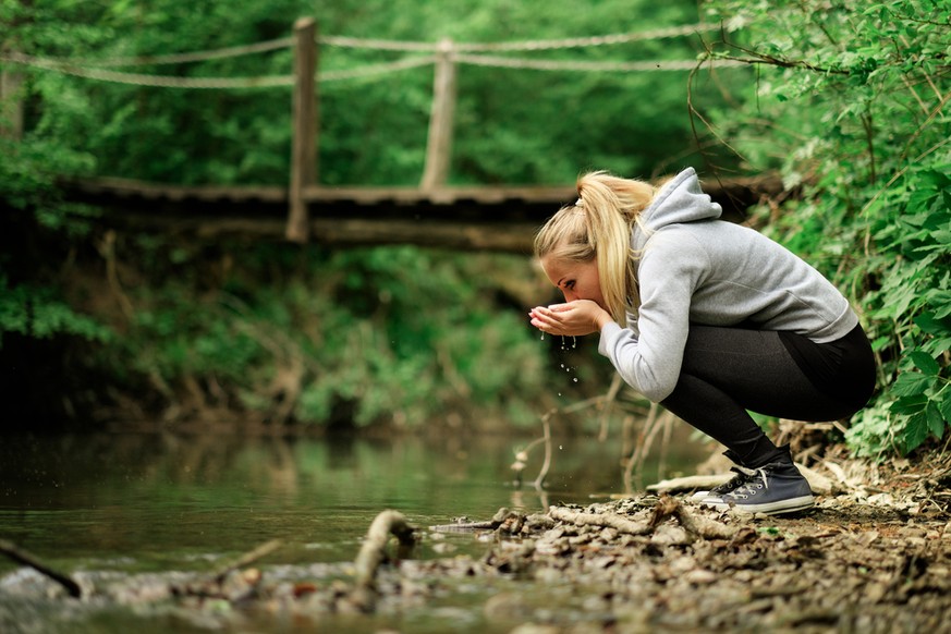 Frau trinkt Wasser aus einem Bach