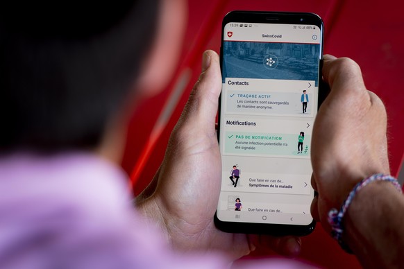 epa08443428 A man looking at a smartphone with the tracing app SwissCovid, using Decentralized Privacy-Preserving Proximity Tracing (DP-3T), during the state of emergency of the coronavirus disease (C ...