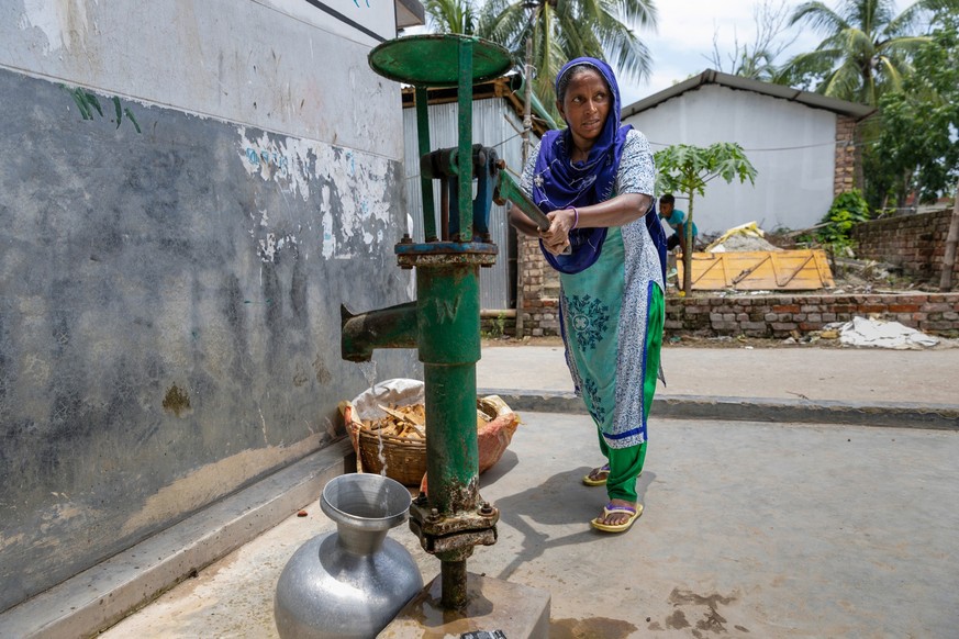 Eine Frau pummpt Wasser im Bastuhara Slum in Bangladesh.