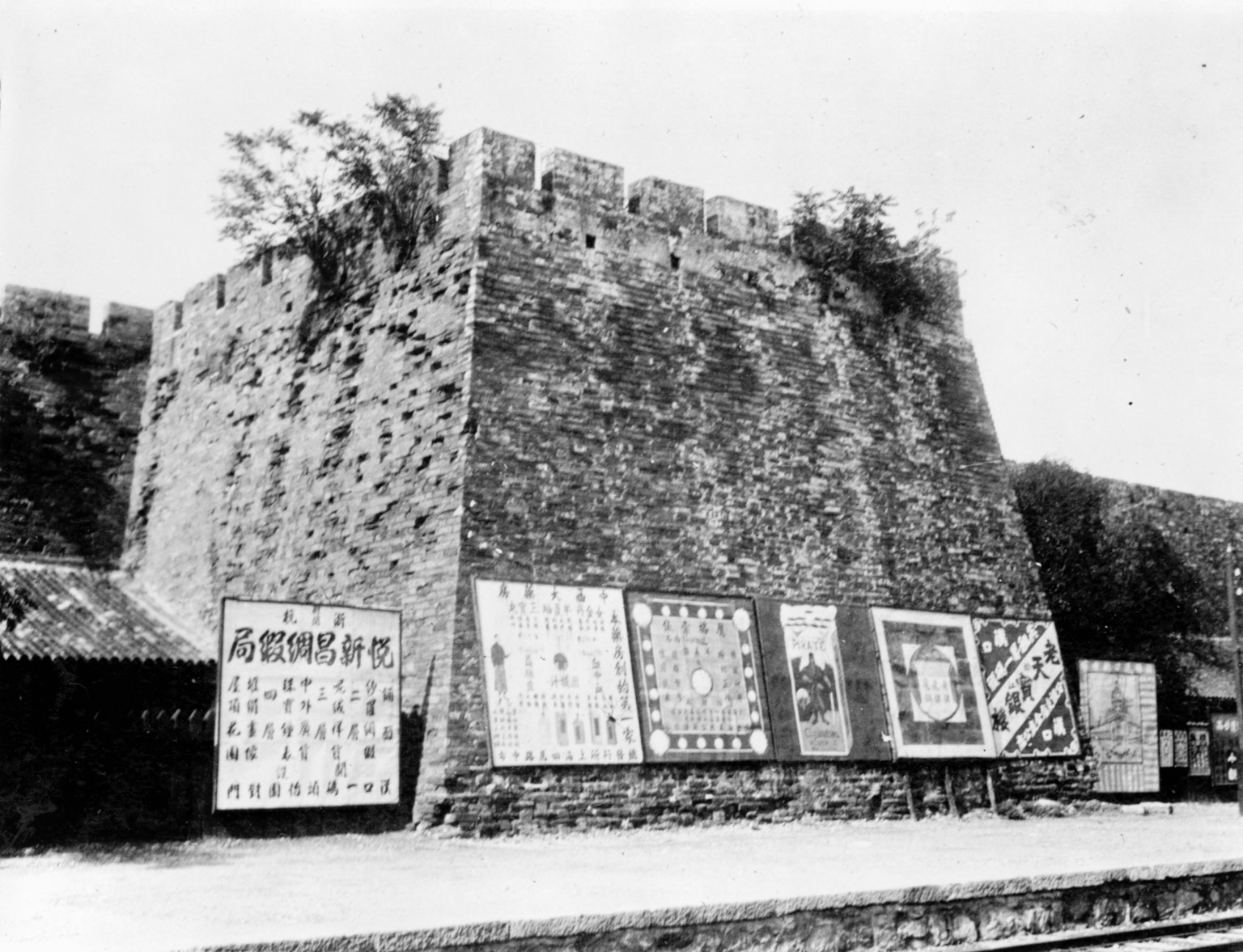 Plakate an der Stadtmauer. Im Vordergrund sind Gleisanlagen sichtbar (um 1900).