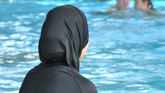 ARCHIV - Eine muslimische Schülerin sitzt am 23.06.2009 in einem Ganzkörper-Badeanzug (Burkini) am Rande eines Schwimmbeckens. Zwei muslimische Eltern aus Basel wehren sich vor dem Europäischen Mensch ...