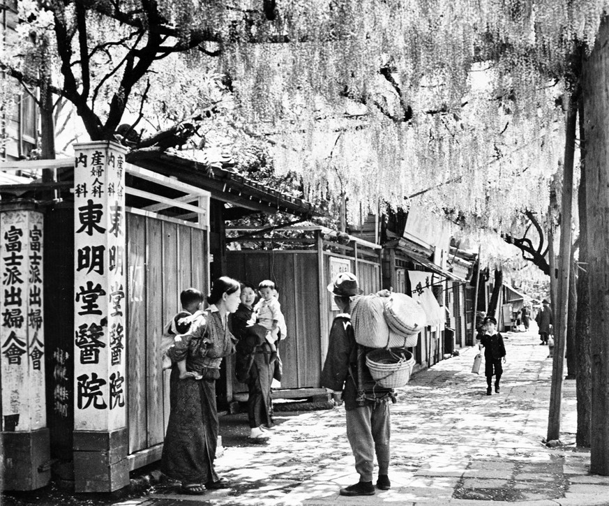 Wisteria hang down in clusters over a residential street where women are shown with their children in the Keishagawa area in Tokyo, Japan, July 30, 1941. (AP Photo)