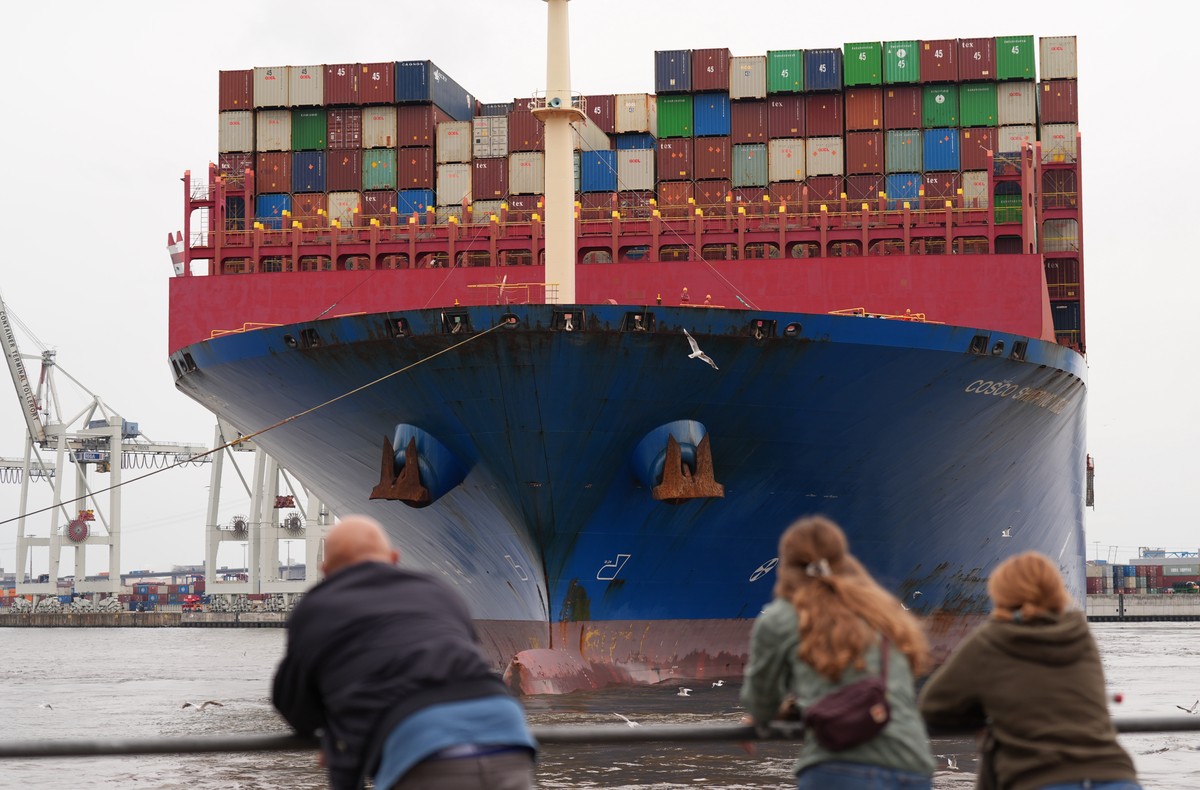 dpatopbilder - 21.07.2025, Hamburg: Passanten verfolgen das Anlegeman�ver des riesigen Containerschiffs �Cosco Shipping Virgo� der Reederei Cosco Shipping, w�hrend es im Hamburger Hafen von Schleppern ...