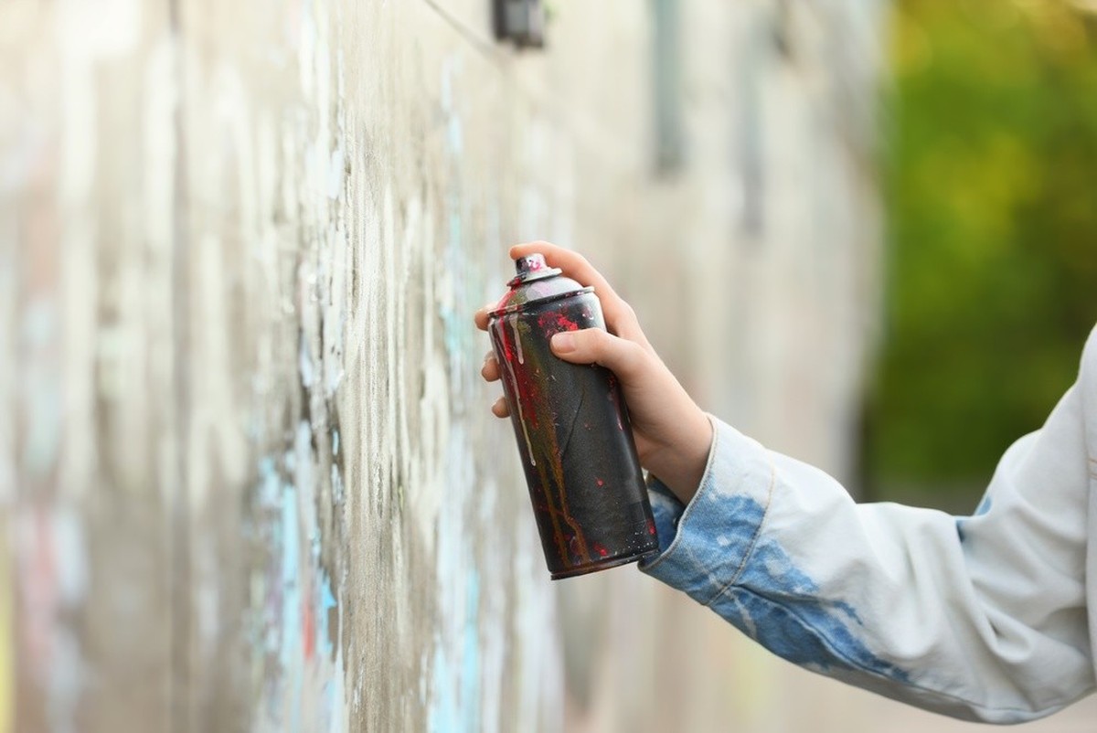 Une personne utilise une bombe de peinture pour réaliser un graffiti sur un mur en béton, dans un environnement urbain extérieur.