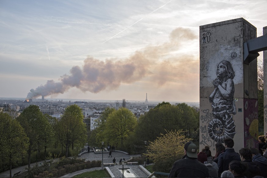 People watch Notre Dame cathedral burning in Paris, Monday, April 15, 2019. Massive plumes of yellow brown smoke is filling the air above Notre Dame Cathedral and ash is falling on tourists and others ...