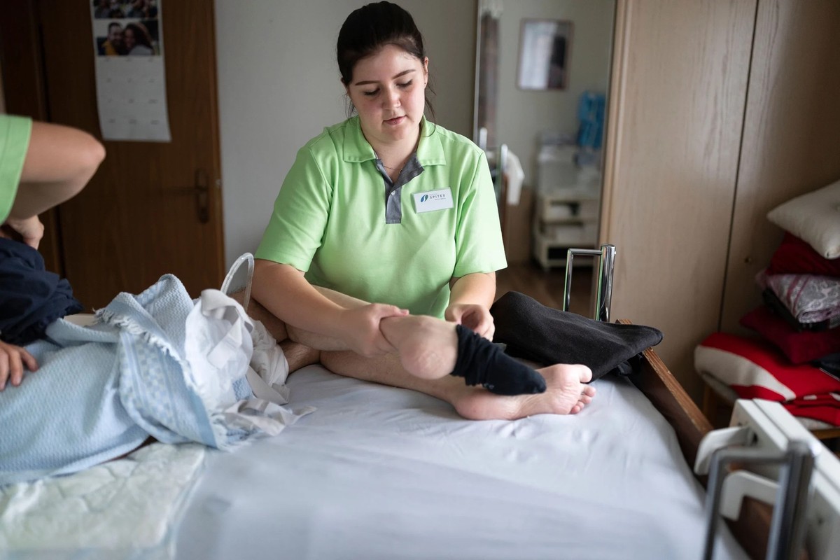 Une apprentie assistante en soins et santé communautaire habille un patient: son salaire est revalorisé grâce à l'offensive en matière de formation.