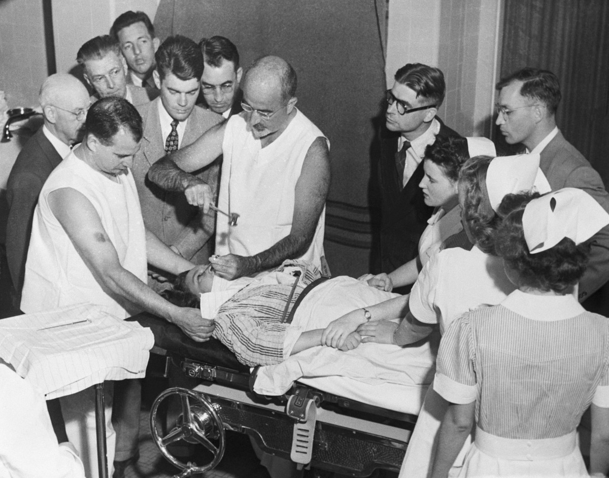 Dr. Walter Freeman performs a lobotomy using an instrument like an ice pick which he invented for the procedure. Inserting the instrument under the upper eyelid of the patient, Dr. Freeman cuts nerve  ...