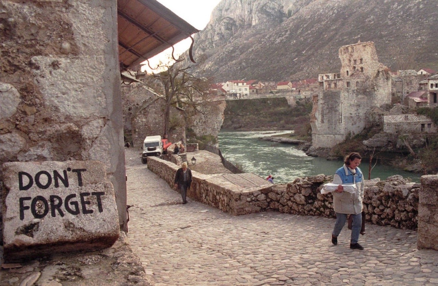 Citizens of Mostar walk at Neretva river bank in front of improvized bridge at place of famous Old Bridge Thursday, November 30, 1995, by the sign reminder of Bosnian Croats made destruction at Muslim ...