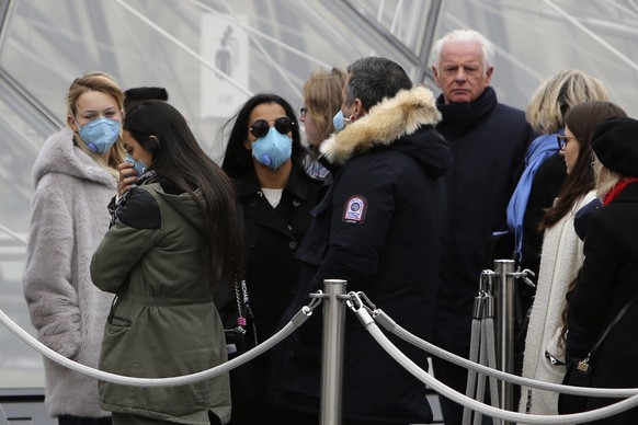 Tourists, some wearing a mask, queue to enter the Louvre museum Friday, Feb. 28, 2020 in Paris. . The world is scrambling to get on top of the new coronavirus outbreak that has spread from its epicent ...