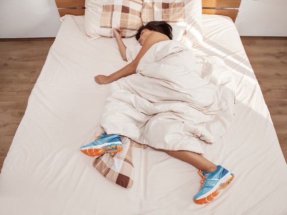 Frau schläft mit Jogging-Schuhen im Bett.