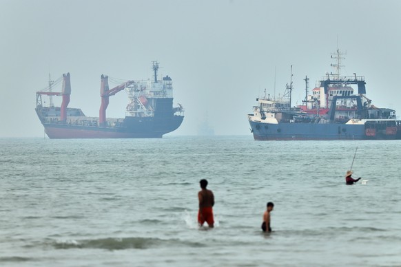 Children wade in the water with cargo ships at anchor in the background and a fisherman nearby, in the Strait of Hormuz off Bandar Abbas, Iran, Tuesday, June 30, 2026. (Amirhosein Khorgooi/ISNA via AP ...
