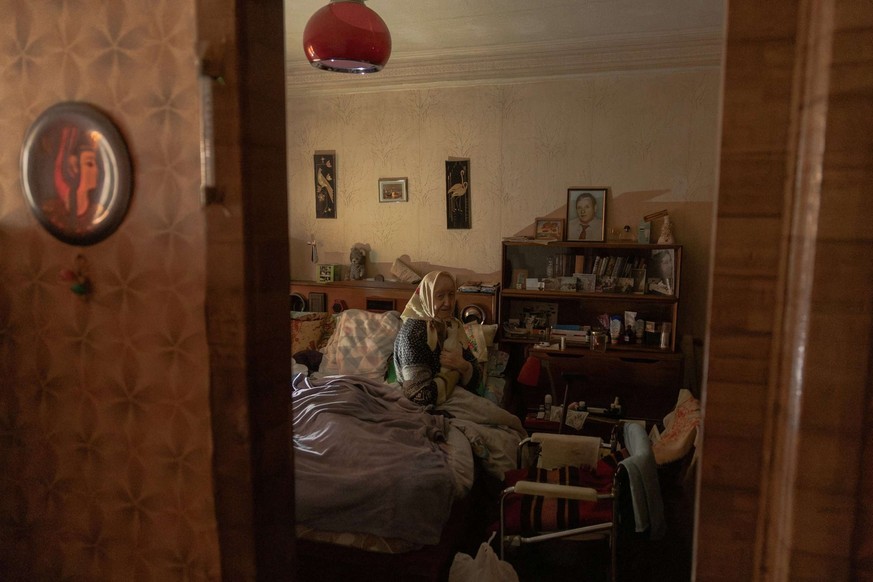 Esfir Rudminska, assise sur un lit dans son appartement sans électricité et presque sans chauffage.