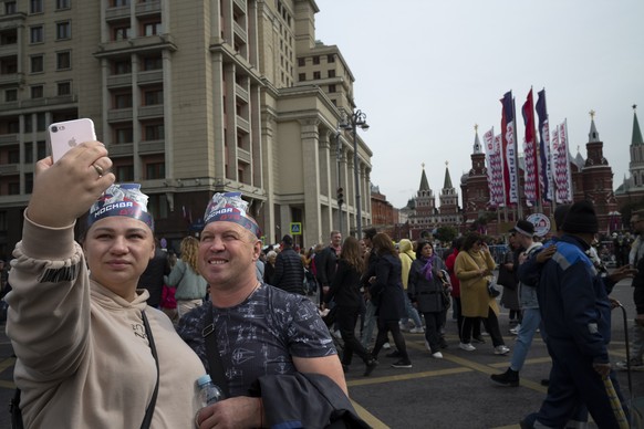 A couple wearing headdresses reading &quot;Moscow 875&quot; pose for selfie on Manezhnaya Square with the Historical Museum, right, and Red Square in the background during celebration of the Moscow Ci ...