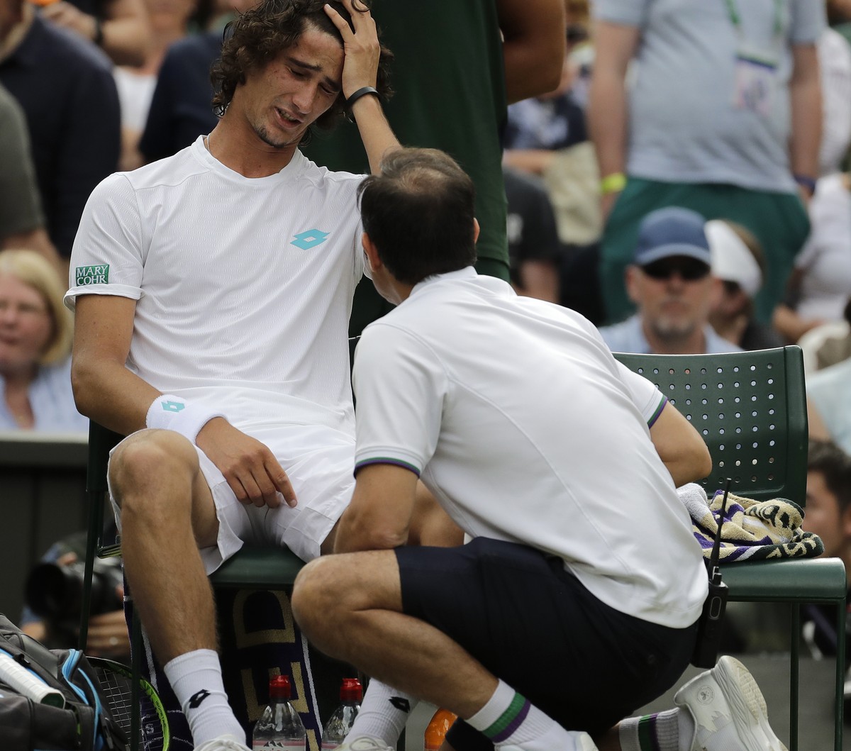 South Africa's Lloyd Harris grimaces as he gets treatment as he plays Switzerland's Roger Federer in a Men's singles match during day two of the Wimbledon Tennis Championships in London ...