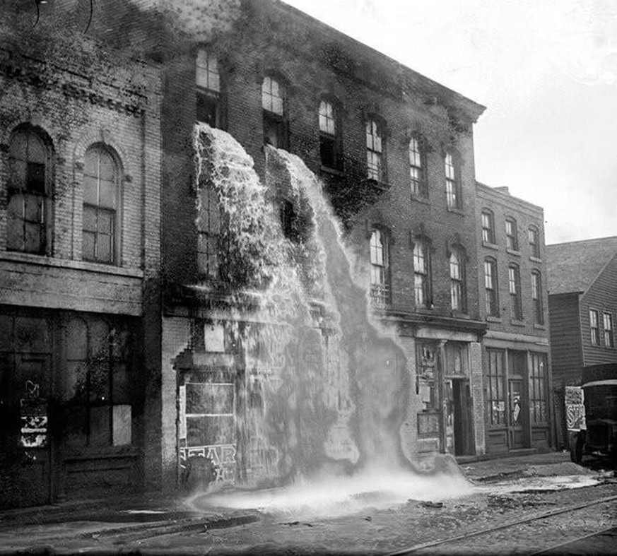 Alcohol, discovered by Prohibition agents during a raid on an illegal distillery, pours out of upper windows of a three story storefront in Detroit during Prohibition (1929)