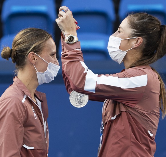 Switzerland's Belinda Bencic, right, hands over the silver medal to her teammate Viktorija Golubic during the women's tennis doubles gold medal match against Barbora Krejcikova and Katerina ...