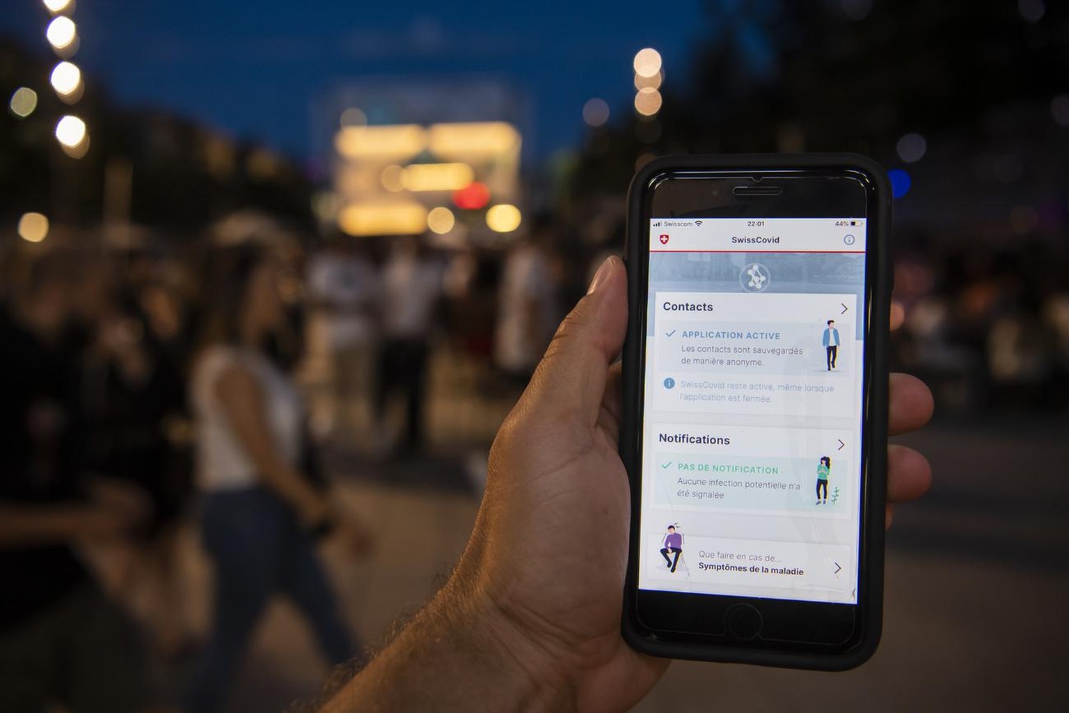 Une personne regarde sur son smartphone l'application SwissCovid alors que des personnes font la fete lors d'une soiree d'ete le samedi 27 juin 2020 dans le quartier du Flon a Lausanne. SwissCovid est ...