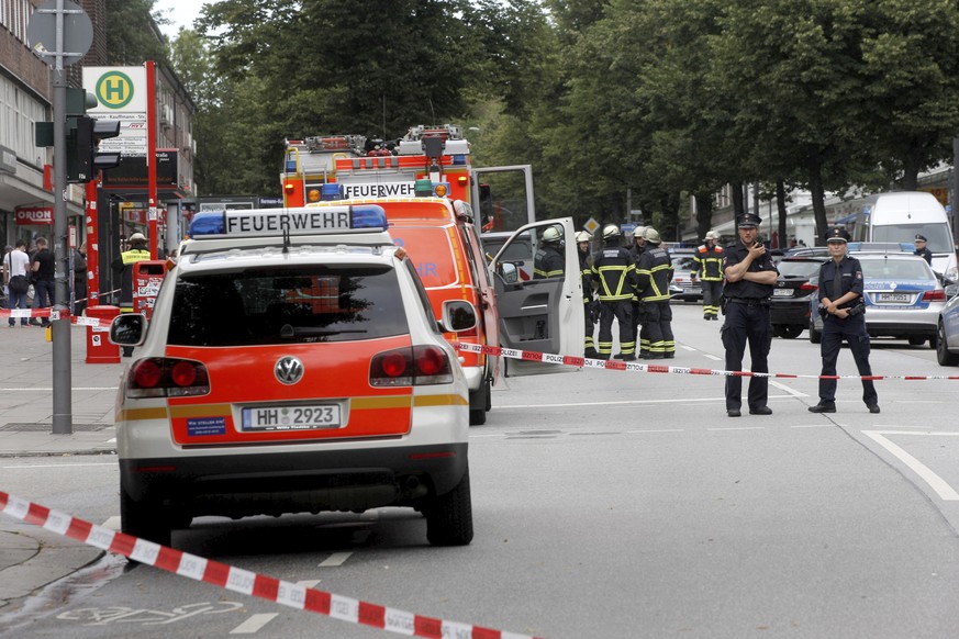 Police officers and fire engines stand in front of the supermarket in Hamburg, Germany, Friday, July 28, 2017, where a man with a knife fatally stabbed one person and wounded four others as he fled, p ...