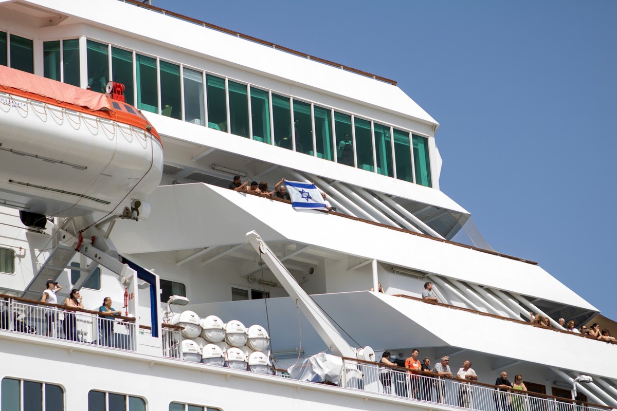 epa12269043 Israeli tourists hold their national flag as the cruise ship 'Iris Crown' arrives at the port of Rhodes, Greece, 28 July 2025. Protesters held a demonstration at the port, expres ...