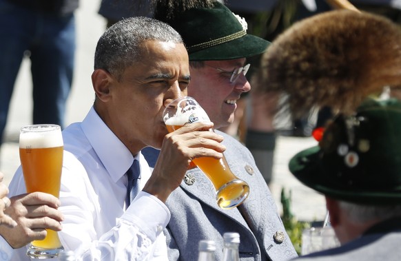U.S. President Barack Obama drinks a beer as he sits between men dressed in traditional Bavarian clothes during a visit to the village of Kruen, southern Germany, Sunday, June 7, 2015 prior to the G-7 ...
