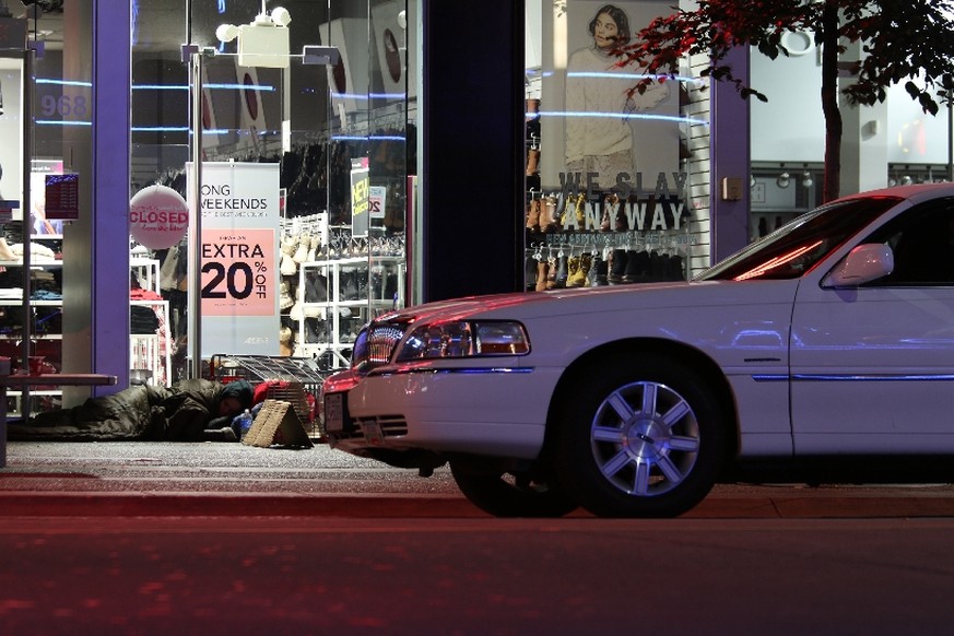 Ein Limousine lädt Männer in Anzügen sowie Frauen in Highheels aus, während ein paar Meter daneben Menschen auf der Strasse schlafen.