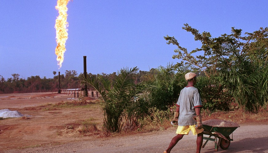 390464 36: A villager walks past a column of fire from the Oshie flare station owned by Italian oil company Agip, March 8, 2001 near Akaraolu, Nigeria. The natural gas flare was lit in 1972 and has be ...
