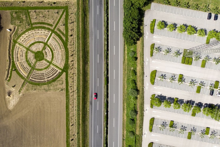 A field with a permaculture mandala garden, a project of Le Rosey boarding school, is depicted next to a car driving on the A1, downtown, and an empty parking lot, right, during the...