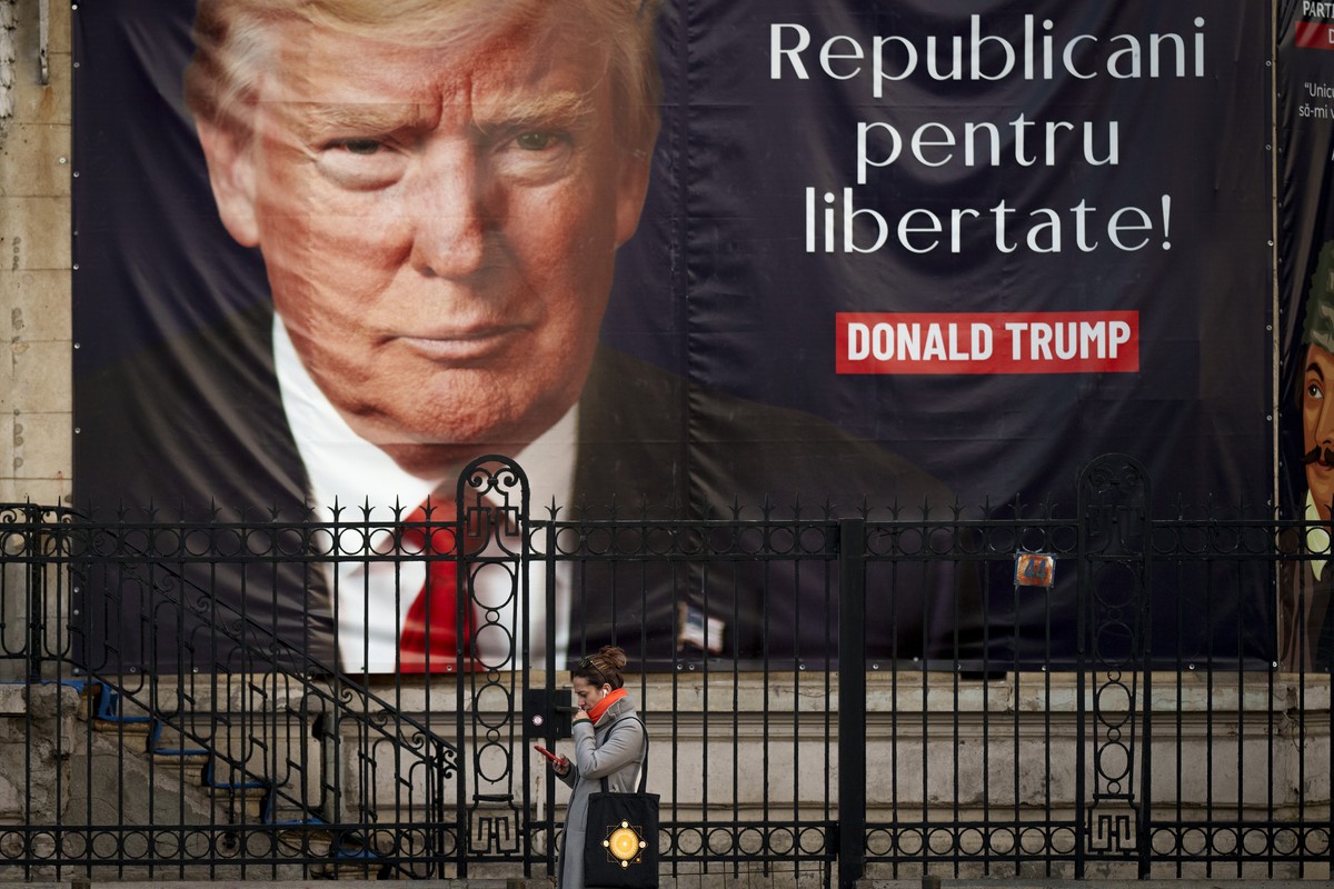 A woman looks at a mobile phone in front of a large banner that reads "Republicans for Freedom" showing U.S. President-elect Donald Trump on the building of a political party in Bucharest, R ...
