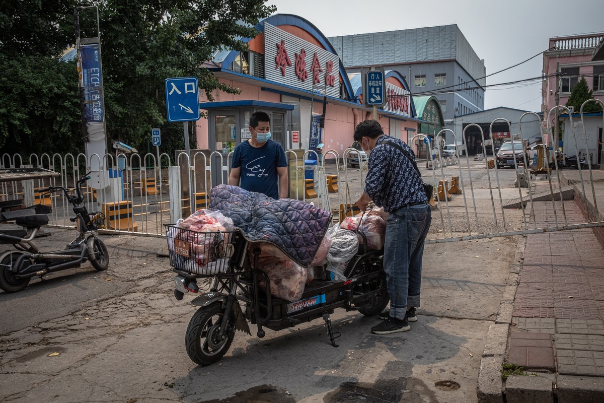 epa08482083 Men wearing protective face masks load a scooter with meat next next to the closed Xinfadi market building in Fengtai district, Beijing, China, 13 June 2020. One of Beijing's largest  ...
