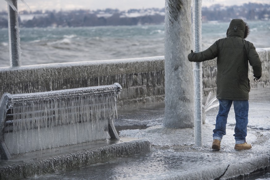 Une personne marche a cote d&#039;un banc ensevelie par la glace se formant suite au vent fort au bord du lac Leman ce mardi 17 janvier 2017 a Versoix dans le canton de Geneve. (KEYSTONE/Jean-Christop ...