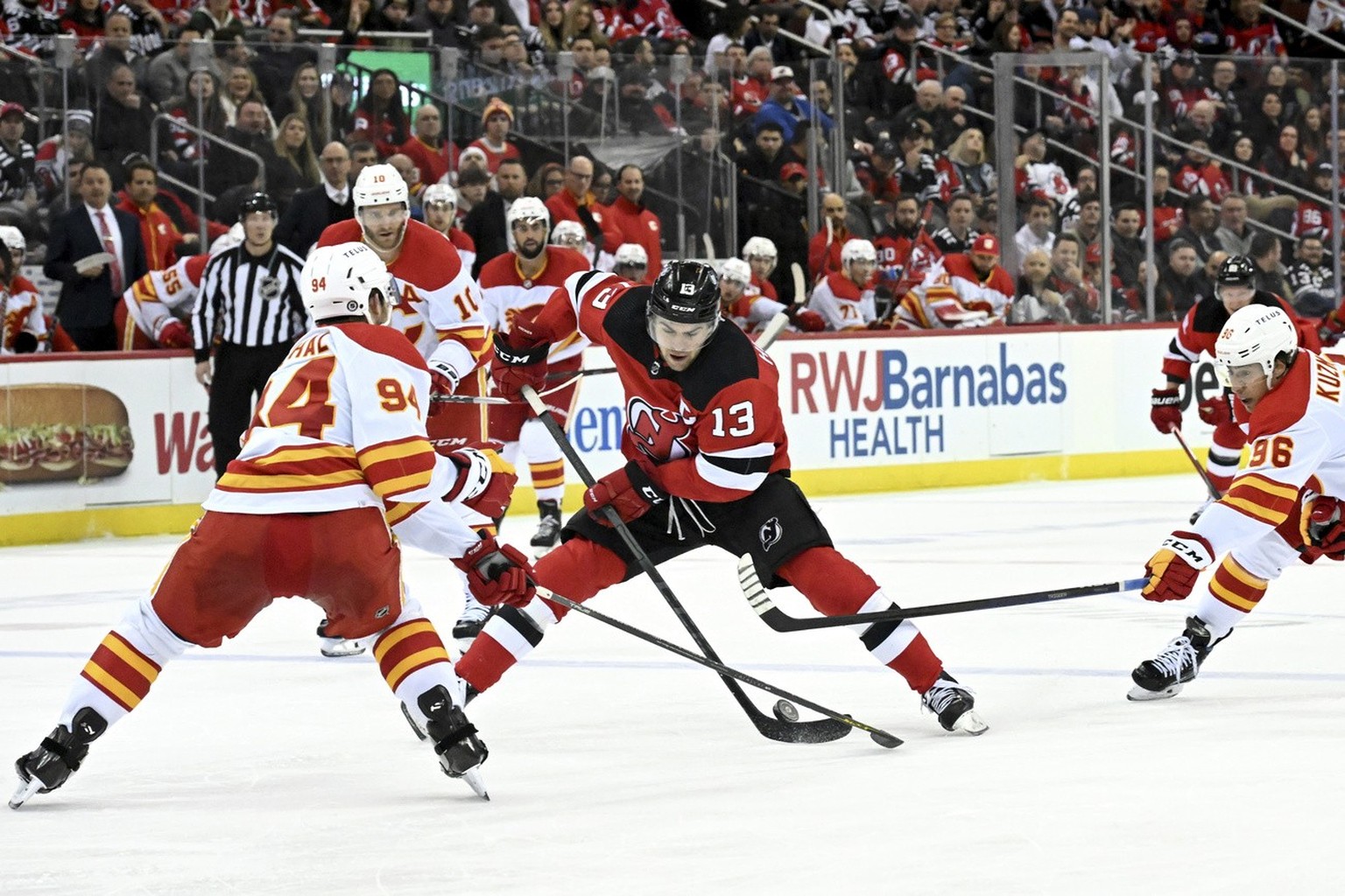 New Jersey Devils center Nico Hischier (13) controls the puck as he is pressured by Calgary Flames&#039; Brayden Pachal (94) and Andrei Kuzmenko, right, during the second period of an NHL hockey game  ...