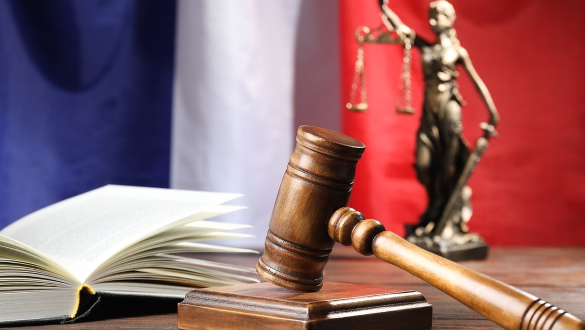 Gavel du juge, livre et statue de la Justice sur une table en bois, avec le drapeau français en arrière-plan.