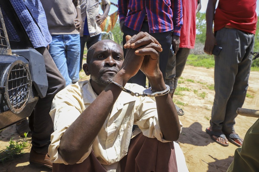 An unidentified man sits in handcuffs after being arrested accused of having connections with pastor Paul Makenzi, in a forest near the village of Shakahola, near the coastal city of Malindi, in south ...