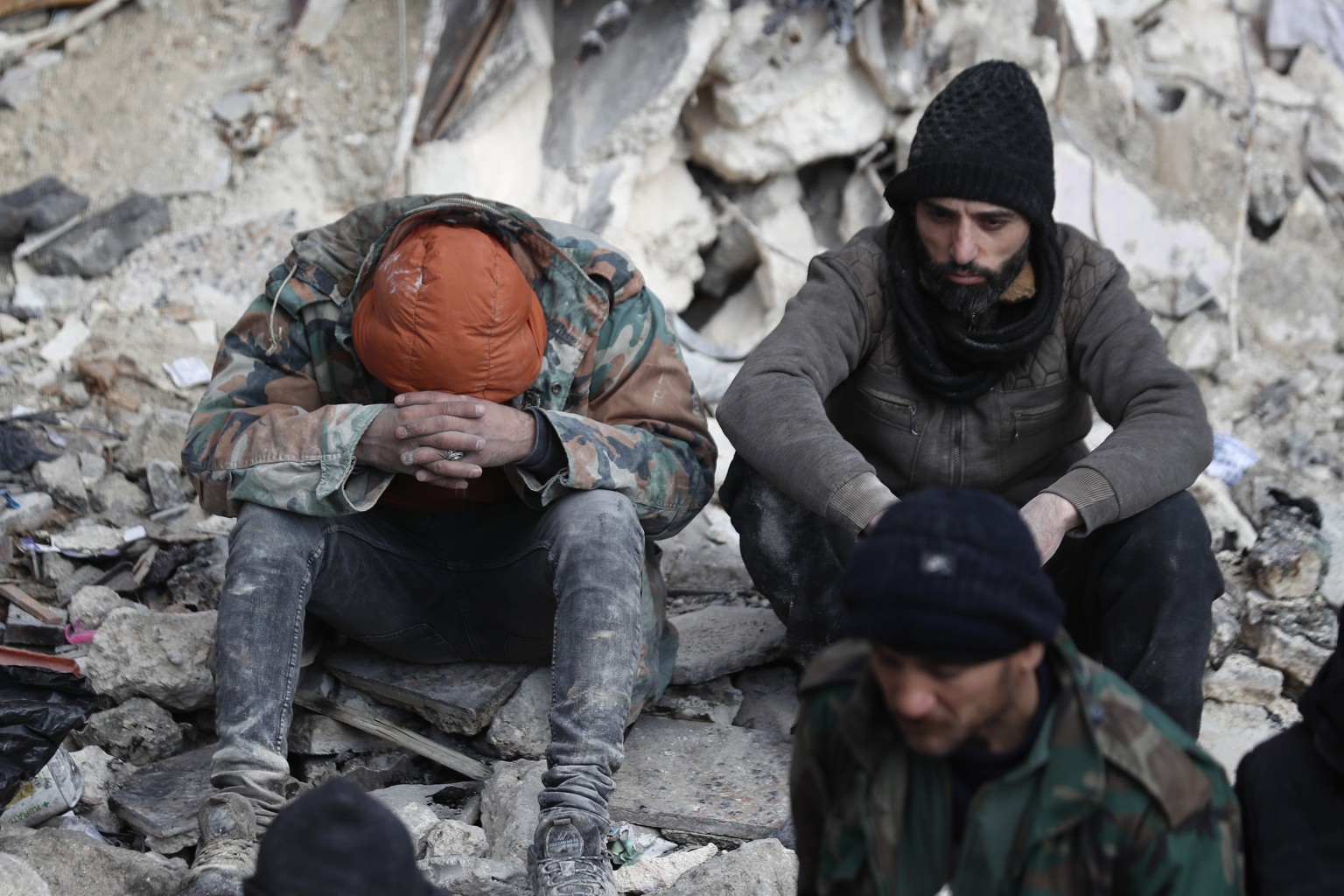 People react as they sit on the wreckage of collapsed buildings, in Aleppo, Syria, Tuesday, Feb. 7, 2023. Rescuers raced Tuesday to find survivors in the rubble of thousands of buildings brought down  ...