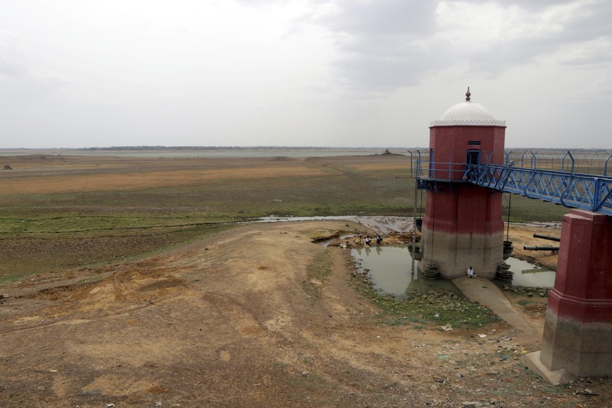 People rest by a measuring tower in the dried-up puzhal reservoir on the outskirts of Chennai, capital of the southern Indian state of Tamil Nadu, Wednesday, June 19, 2019. Millions of people are turn ...