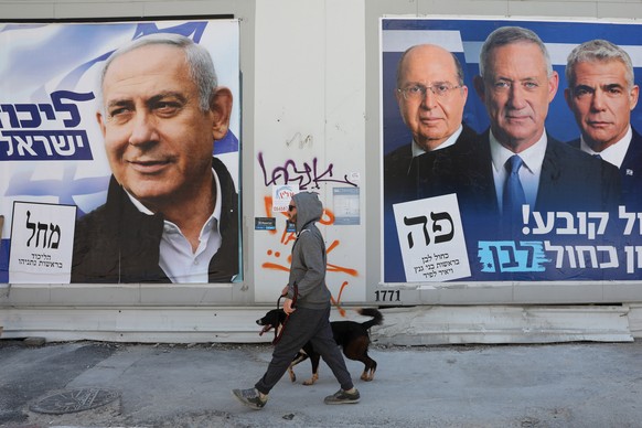 epa07482273 A man walks with his dog between election campaign billboards of Prime Minister and leader of the Likud party Benjamin Netanyahu (L) and leaders of the Blue and White party Benny Gantz (2- ...
