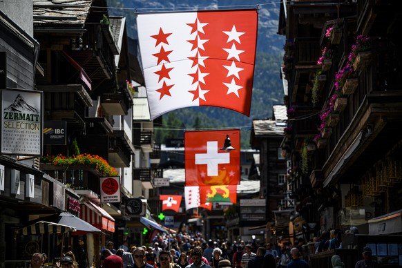 Des touristes visitent la rue centrale du village de montagne sous le drapeau du canton du Valais et sous le drapeau Suisse le vendredi 17 juin 2022 a Zermatt. (KEYSTONE/Jean-Christophe Bott)