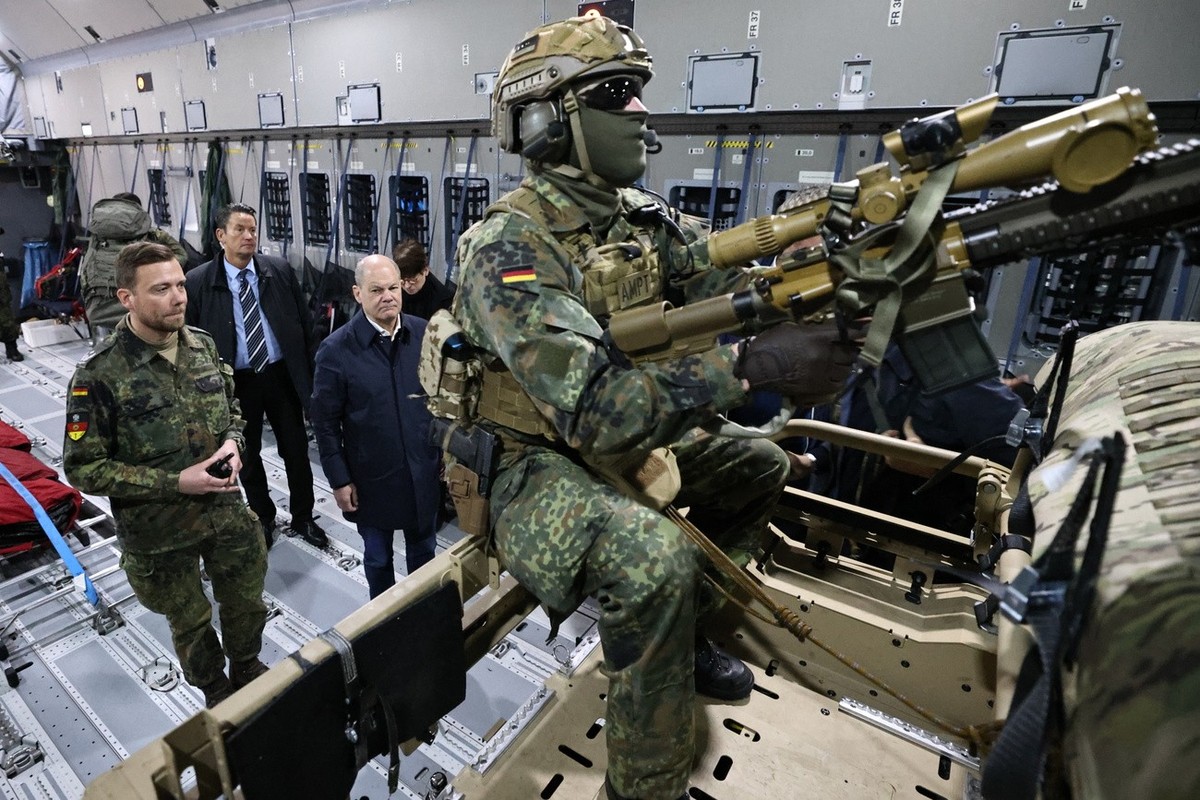 epa10933912 German Chancellor Olaf Scholz (3-L) stands behind a soldier with a machine gun on top of a buggy of the air mobile protection team during a flight in an A400M Airbus from BER government te ...