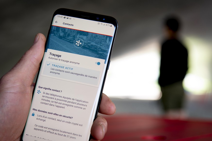 epa08443426 A man looking at a smartphone with the tracing app SwissCovid, using Decentralized Privacy-Preserving Proximity Tracing (DP-3T), during the state of emergency of the coronavirus disease (C ...