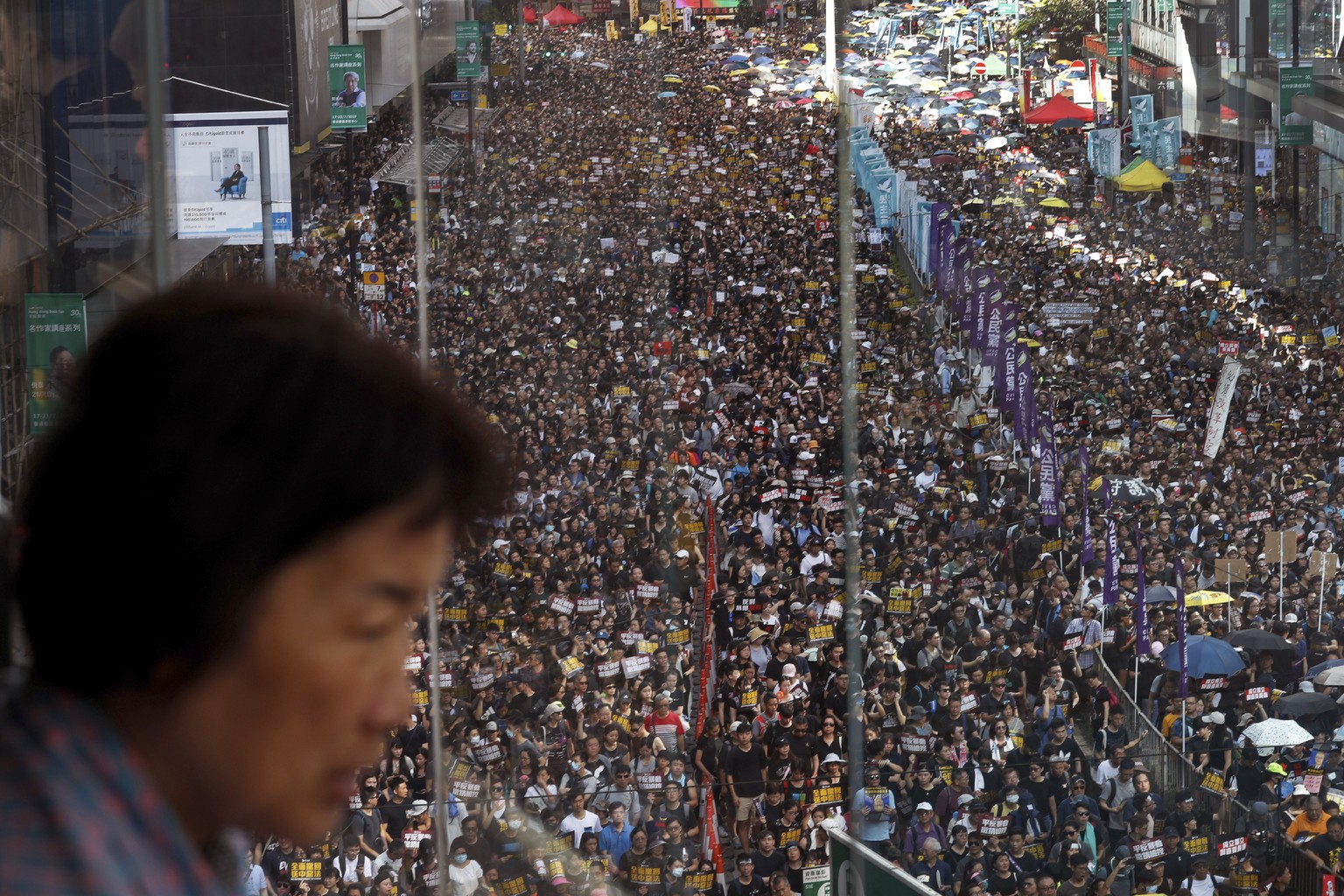 A woman watches protesters march on a street in Hong Kong, Sunday, July 21, 2019. Thousands of Hong Kong protesters marched from a public park to call for an independent investigation into police tact ...