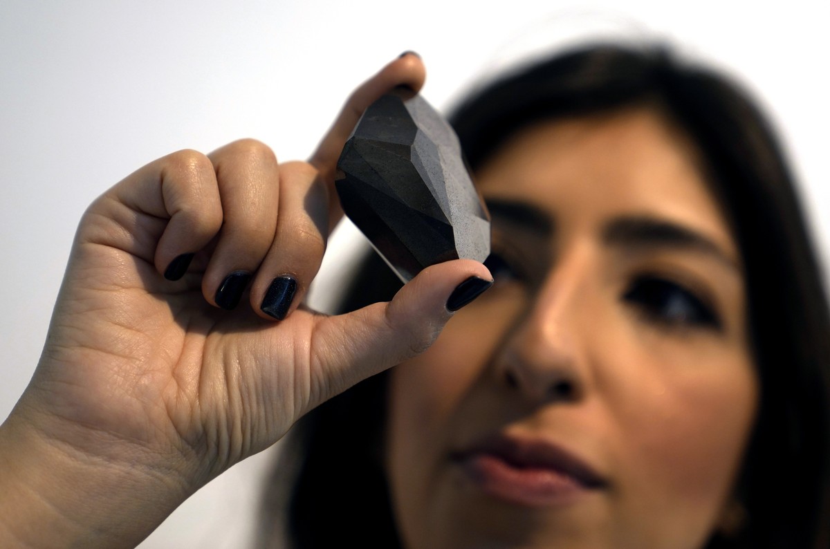 An employee of Sotheby's Dubai presents a 555.55 Carat Black Diamond "The Enigma" to be auctioned at Sotheby's Dubai gallery, in Dubai, United Arab Emirates, Monday, Jan. 17, 2022. ...