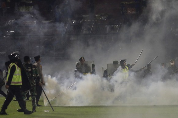 Police officers and soldiers stand amid tear gas smoke during a soccer match at Kanjuruhan Stadium in Malang, East Java, Indonesia, Saturday, Oct. 1, 2022. Clashes between supporters of two Indonesian ...