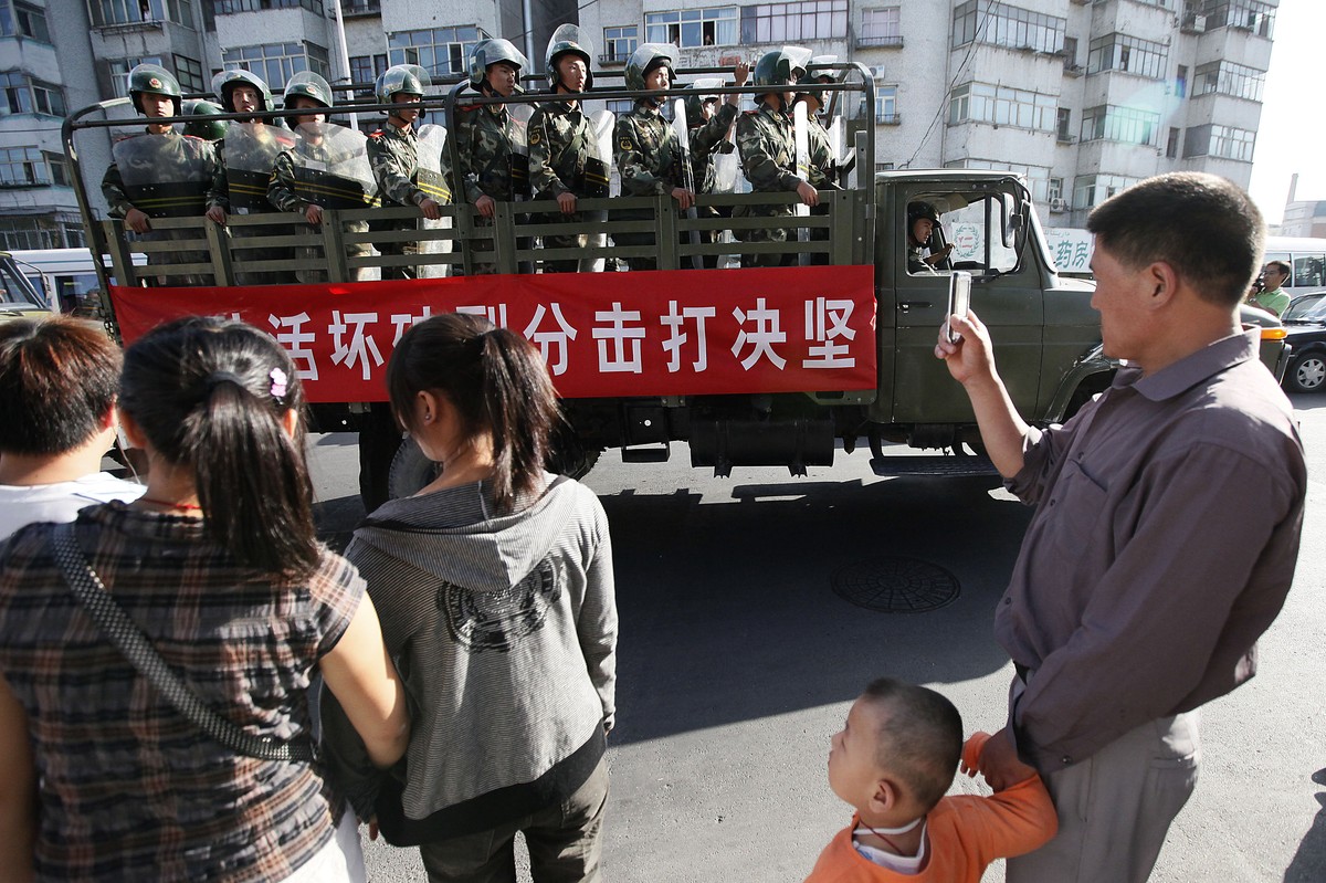 FILE - In this file photo taken Thursday, July 9, 2009, bystanders look at a truckload of paramilitary police with a banner which reads "Determined crackdown on separatist activities" patrol ...