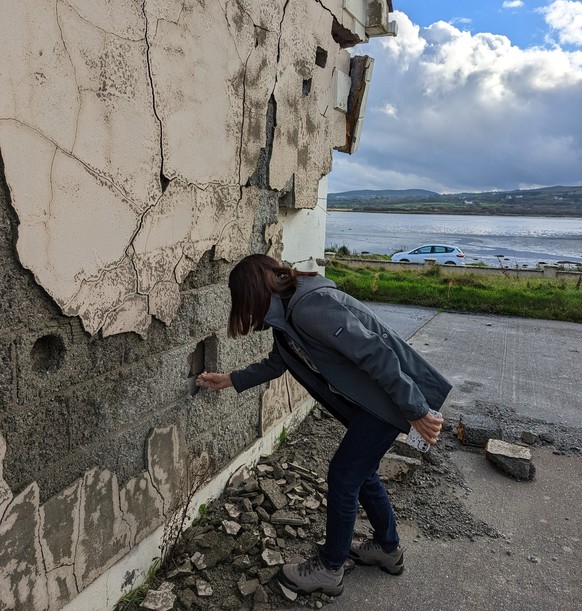 A woman breaks off a piece of concrete from a house in Donegal.  The building can no longer be saved.