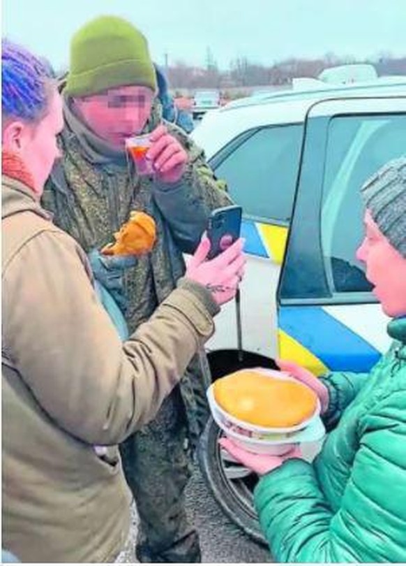 Ein russischer Soldat wird von Ukrainerinnen mit Tee und Brot versorgt.