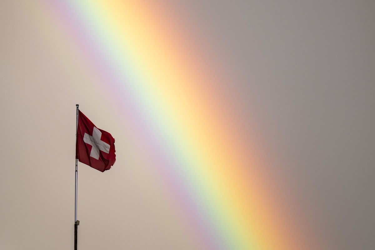 Un arc-en-ciel est visible a cote d'un drapeau suisse lors d'une soiree pluvieuse le vendredi 12 juillet 2024 a Montreux. (KEYSTONE/Jean-Christophe Bott)