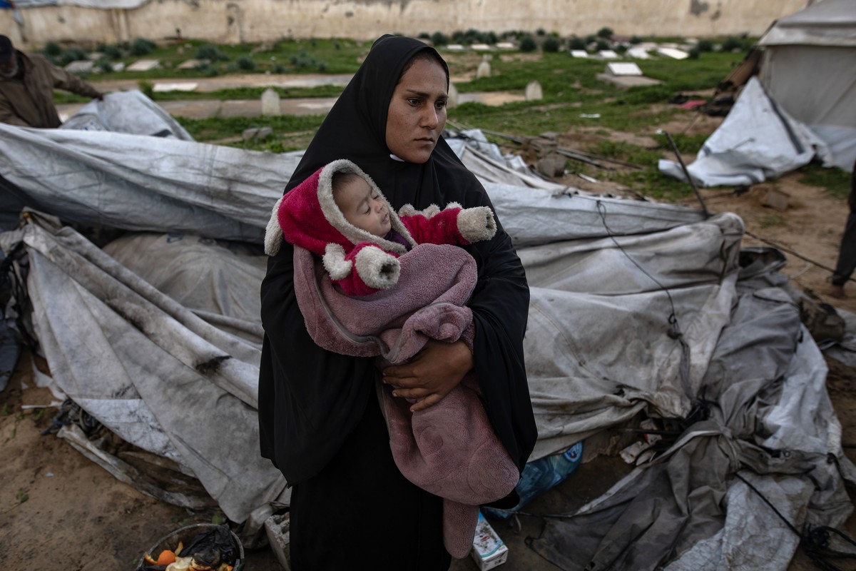 epa12639029 A Palestinian woman carries her infant as her family is trying to gather what remains of their belongings after their tent was damaged in Khan Younis in the southern Gaza Strip, 09 January ...